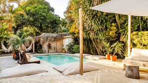 Un área de piscina con sillones reclinables, una estructura de techo de paja y abundante vegetación tropical.