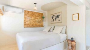 Een slaapkamer met een bed, een wereldkaart aan de muur, een kleine plant en een houten kruk.