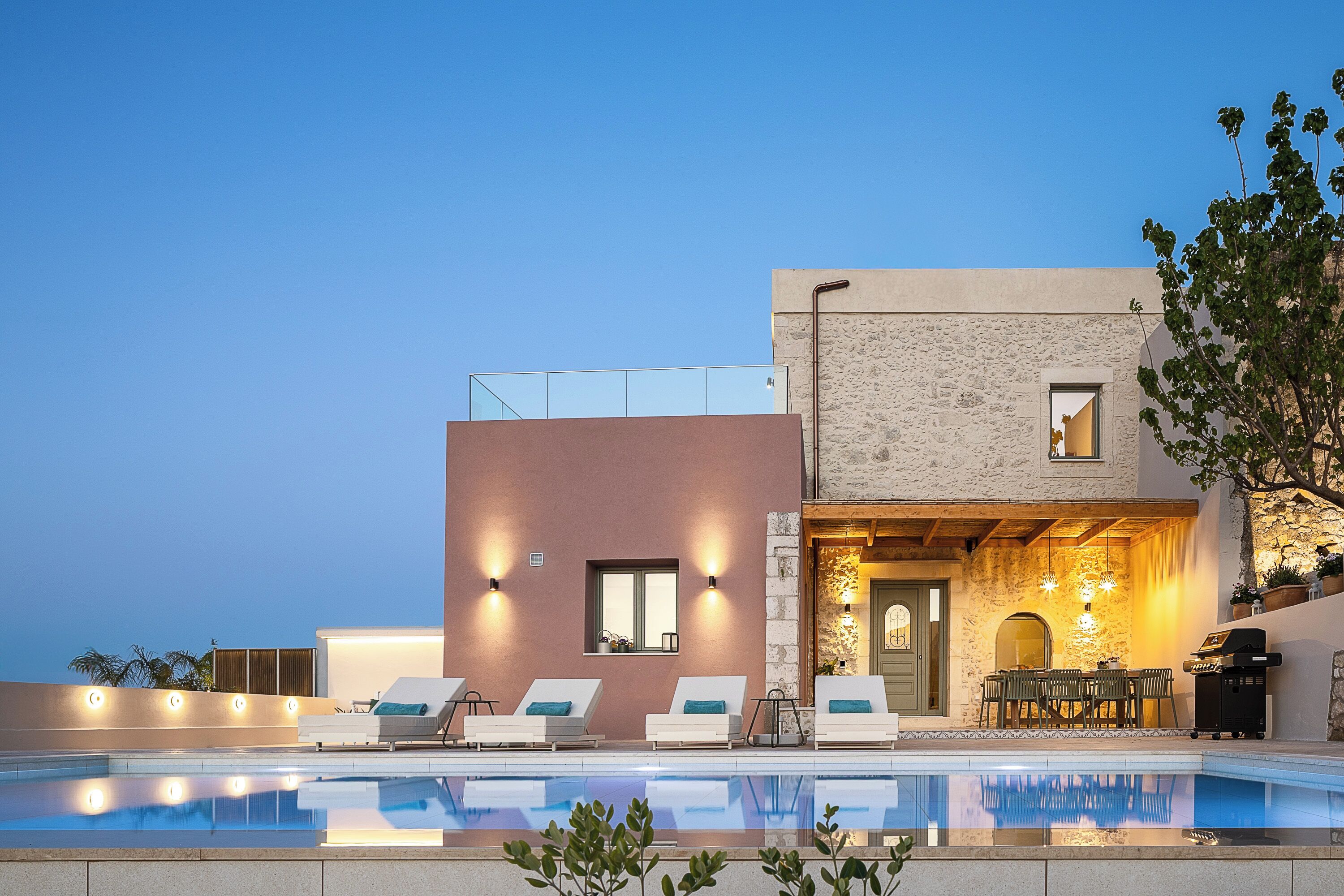 A modern building with a pool, lounge chairs, and outdoor dining area.