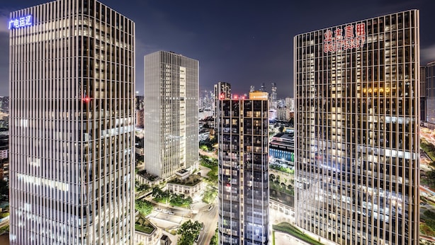 Een hoog gebouw met een modern architectonisch ontwerp, met een gevel in rasterpatroon en verlichte reclameborden.