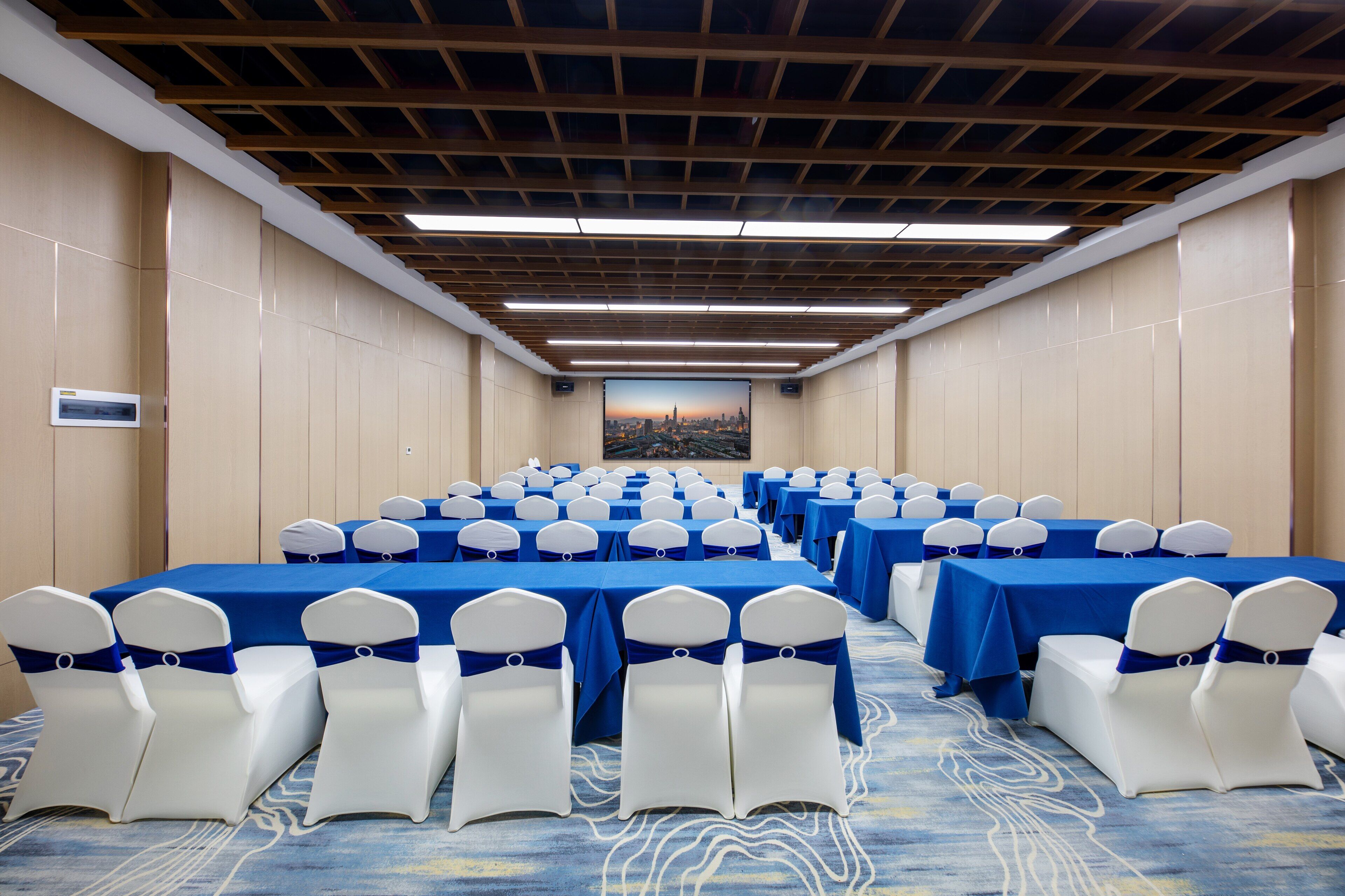 Un salón de conferencias con filas de mesas y sillas, techo de madera y vista panorámica de la ciudad.