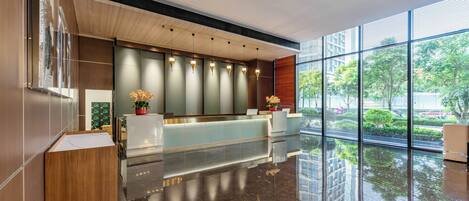 A modern reception area with a wooden reception desk, a glass partition, and a large window offering a view of the outdoors.