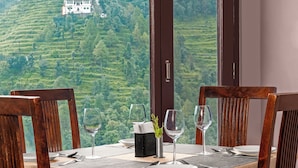 A dining table set with chairs, a vase with a plant, and wine glasses, overlooking a lush green landscape. - BluSalzz Collection Suvaasa - Ramgarh (Ramgarh)