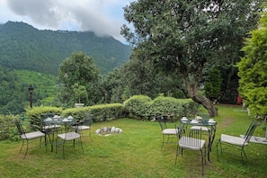 Ein Garten mit rundem Tisch und Stühlen, umgeben von üppiger Vegetation und Blick auf einen Berg.