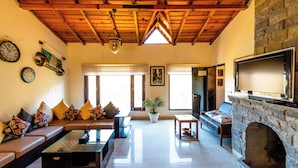 A living room with a stone fireplace, wooden ceiling beams, a sofa with patterned cushions, a coffee table, and a television. - BluSalzz Collection Suvaasa - Ramgarh (Ramgarh)