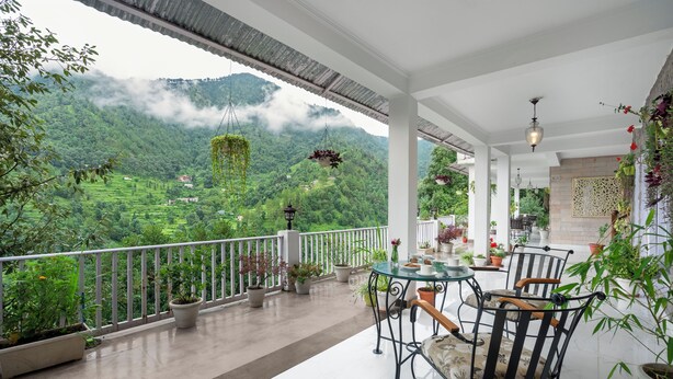 A balcony with a table and chairs, potted plants, and a view of a lush green valley with mountains in the background. - BluSalzz Collection Suvaasa - Ramgarh (Ramgarh)
