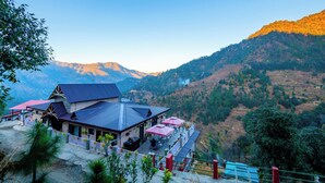 A mountain lodge with a terrace and dining area, surrounded by lush greenery and mountains. - BluSalzz Collection Suvaasa - Ramgarh (Ramgarh)