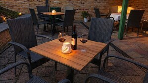 An outdoor patio with wicker chairs and tables, a bottle of wine, and a candle. - Parkside Retreat Central location perfect for couples and families (Bad Muskau)