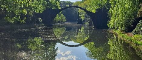 Eine friedliche Flusslandschaft mit einer Steinsbrücke, die sich im Wasser spiegelt, umgeben von üppigem Grün.
