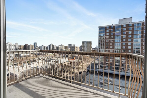 Un balcon offrant une vue sur le paysage urbain, avec de nombreux immeubles et un parking.