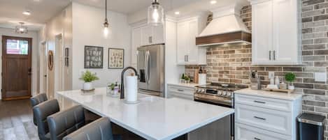 A modern kitchen with white cabinetry, a central island with seating, stainless steel appliances, and a brick accent wall.