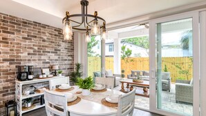 A dining area with a brick wall, a chandelier, and a view of the backyard through large glass doors. - Brand New Home! Downtown Historic District, Private Office, Fully Fenced Yard, $300 in Free Tickets! (St. Augustine)