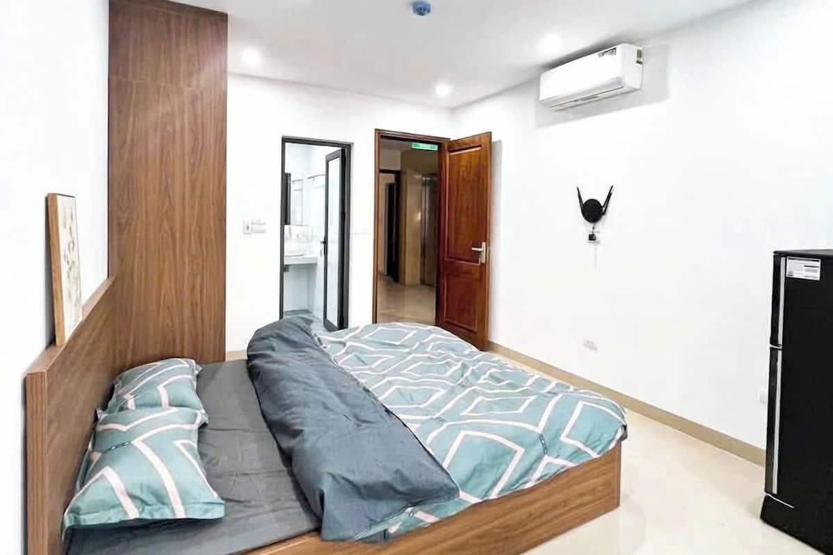 A modern bedroom with a wooden bed frame, a large mirror, and an air conditioning unit on the wall.