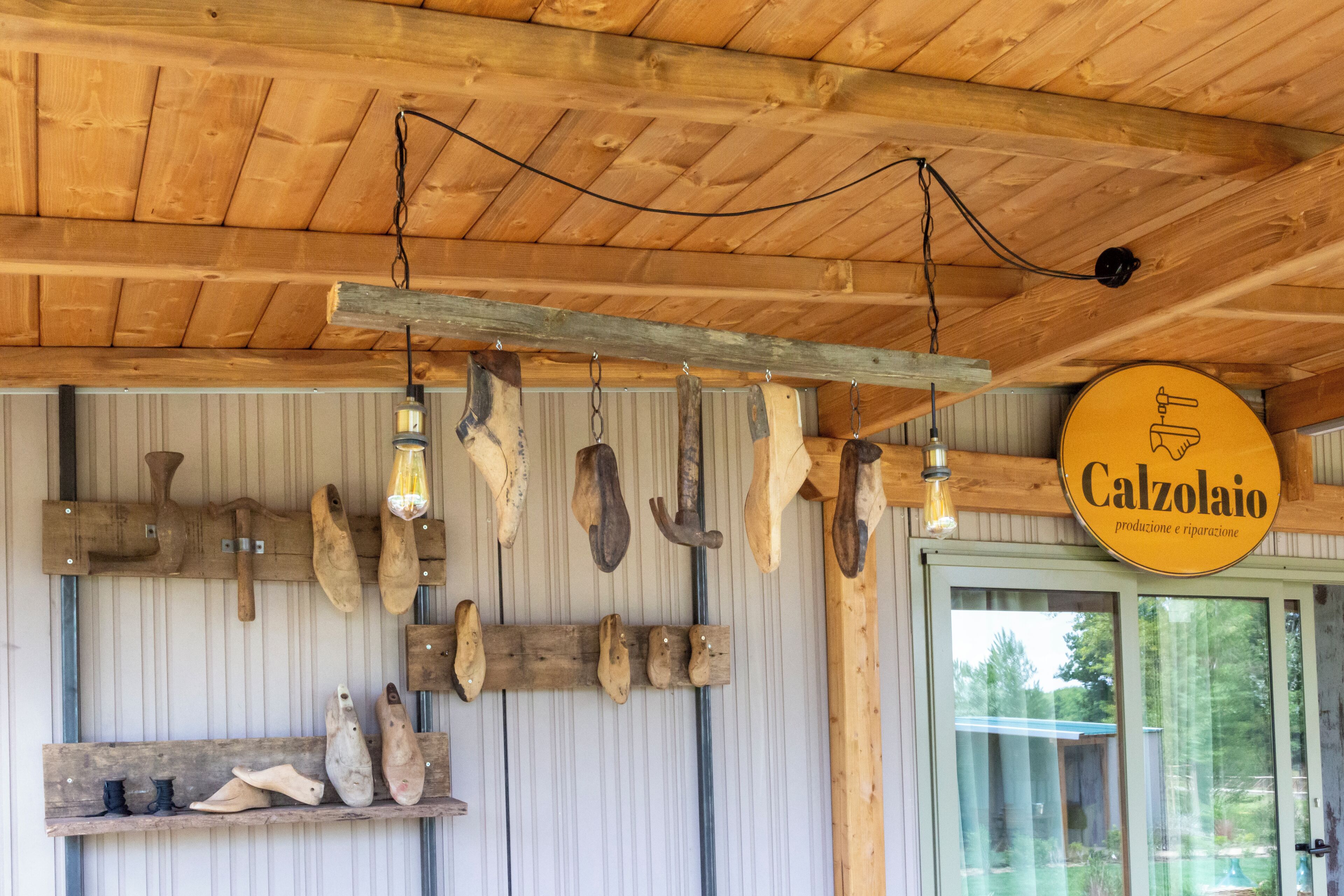 A rustic interior with wooden beams, a hanging light fixture, and a sign reading "Calzolaiio."