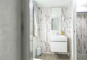 A bathroom with a white sink, mirror, and radiator. There is a trash bin and a shower area visible. -  Palagina Il Borgo Agricolo (Figline e Incisa Valdarno)