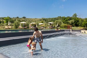 Zona de piscina con sillones de descanso y sombrillas, rodeada de un jardín ajardinado y un paisaje montañoso.