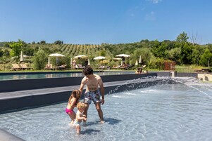 Zona de piscina con sillones de descanso y sombrillas, rodeada de un jardín ajardinado y un paisaje montañoso.