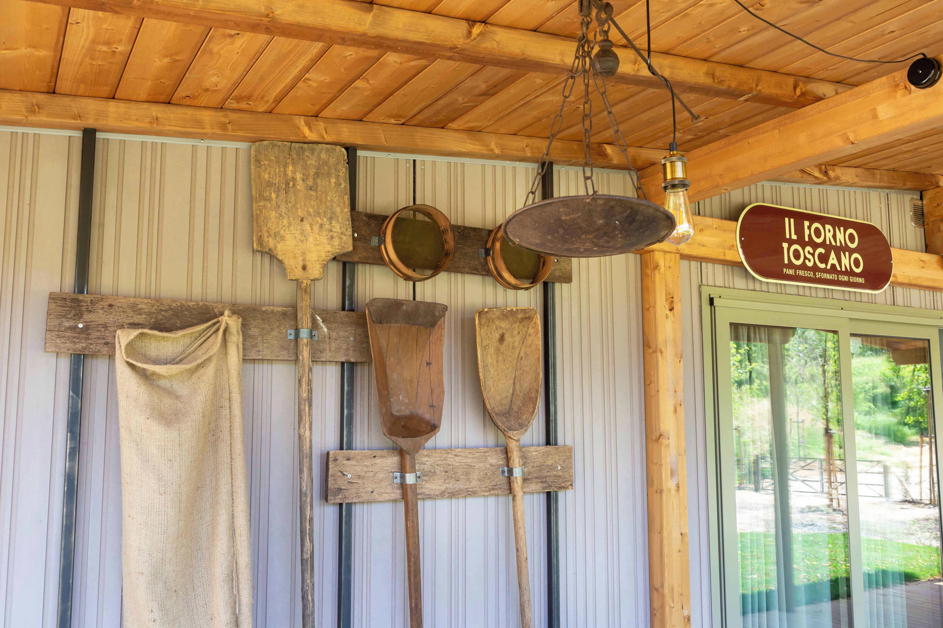 Un intérieur rustique en bois, avec des pagaies en bois et une enseigne sur le mur indiquant « IL FORNO IOSCANO ».