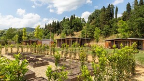 A rural setting with multiple small cabins surrounded by a garden with raised beds and various plants. -  Palagina Il Borgo Agricolo (Figline e Incisa Valdarno)