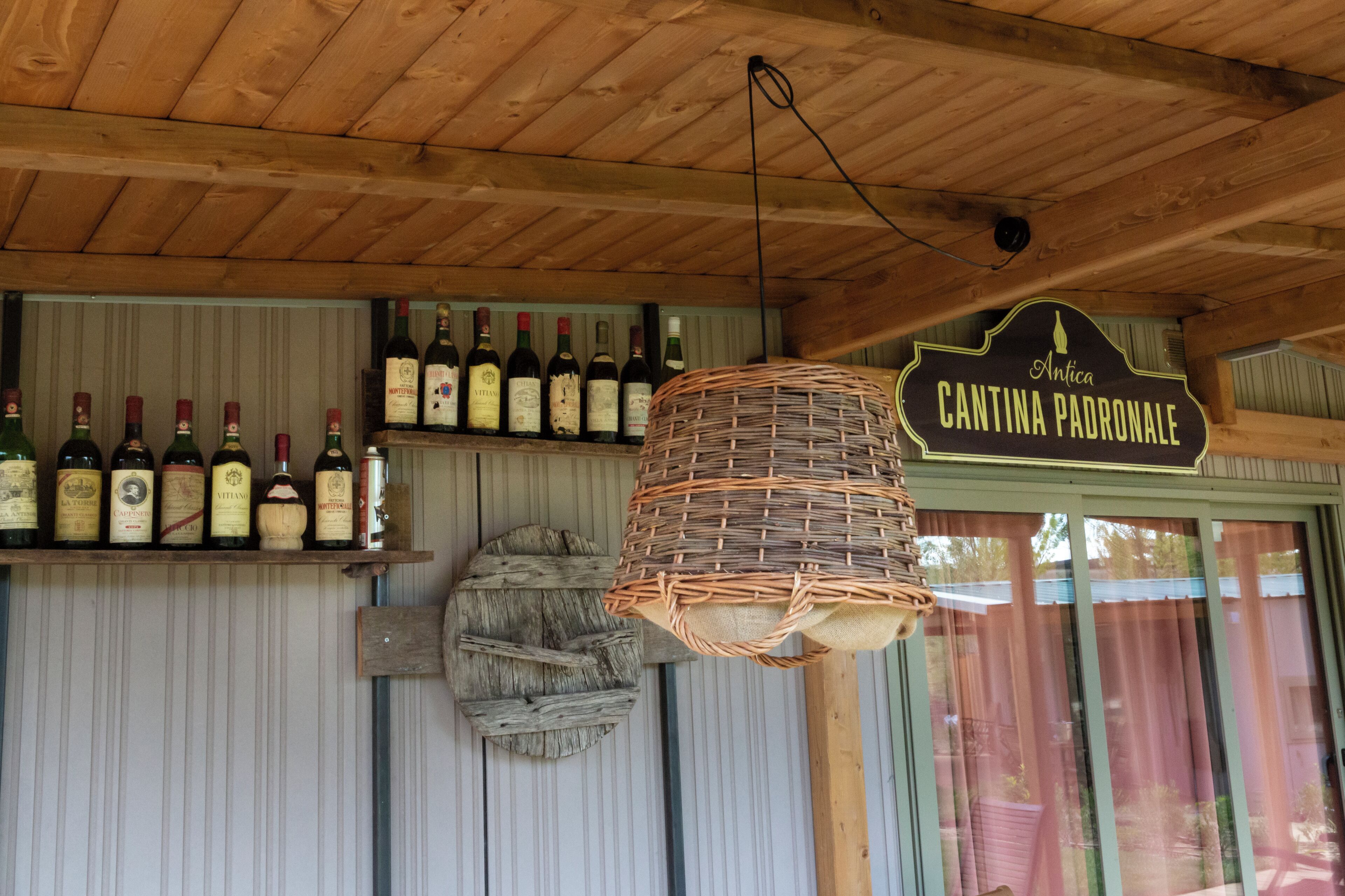 Un interior rústico con vigas de madera, una cesta colgante y una estantería para vinos con botellas.
