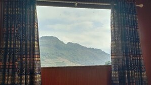 A window with patterned curtains and a view of a mountainous landscape. - Lý Gia Homestay (Quan Ba)