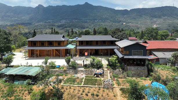 A traditional wooden house with a tiled roof, surrounded by a garden with various plants and a stone wall. - Lý Gia Homestay (Quan Ba)