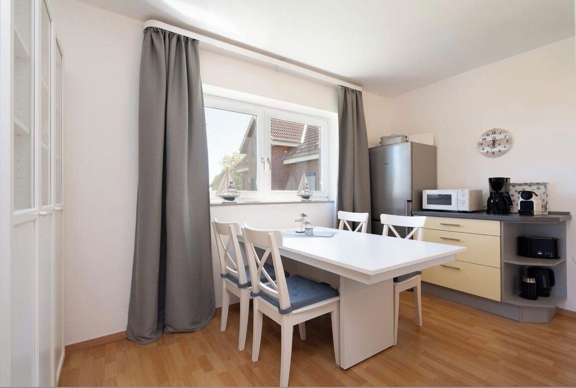 Een kleine keuken met een witte tafel, grijze gordijnen en een magnetron.