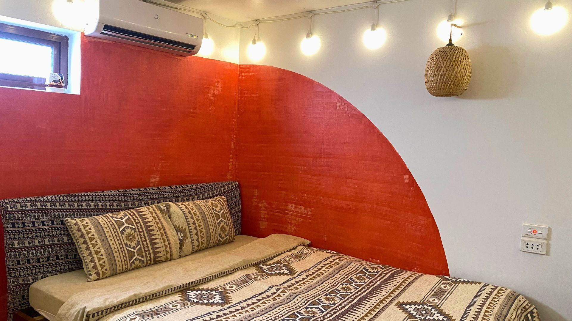 A room with a curved red wall, a patterned bedspread, and a hanging light fixture.