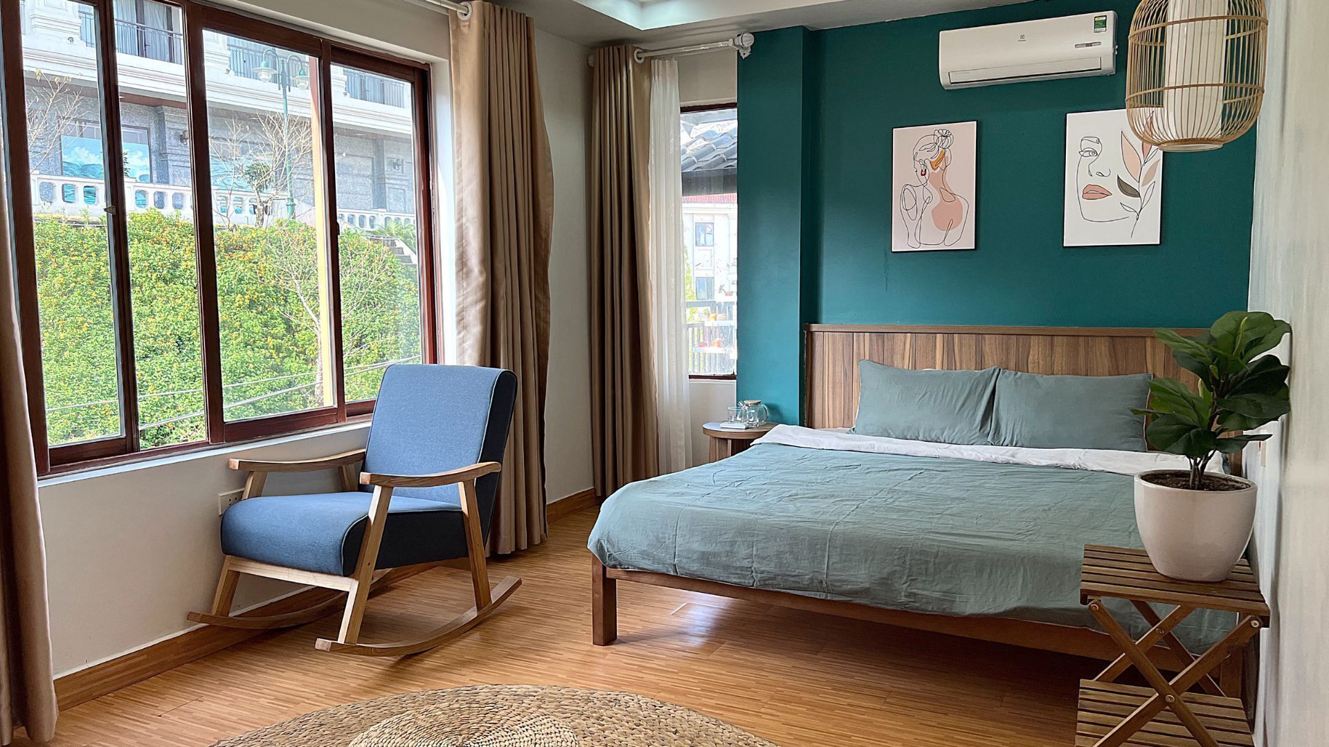 A bedroom with a bed, a rocking chair, a potted plant, and artwork on the wall.