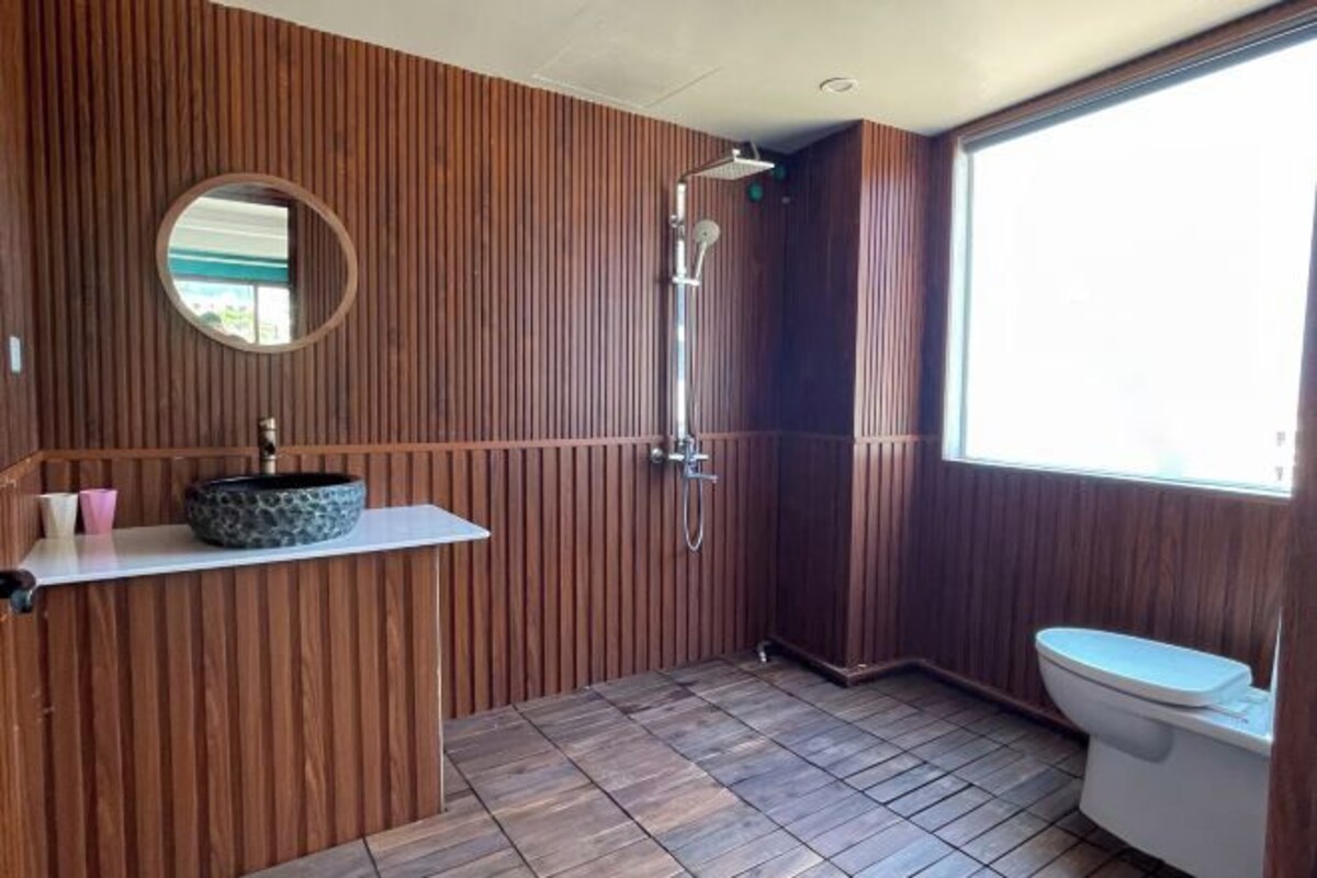 Ein Badezimmer mit Holzvertäfelung, einem runden Spiegel, einem Waschbecken mit runder Schüssel, einer Dusche und einer Toilette.