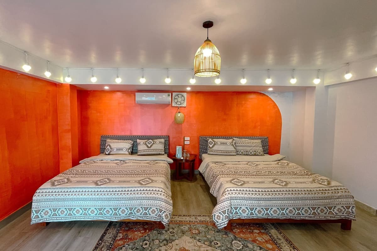 A room with two beds, a hanging light fixture, a wall-mounted fan, and a rug.