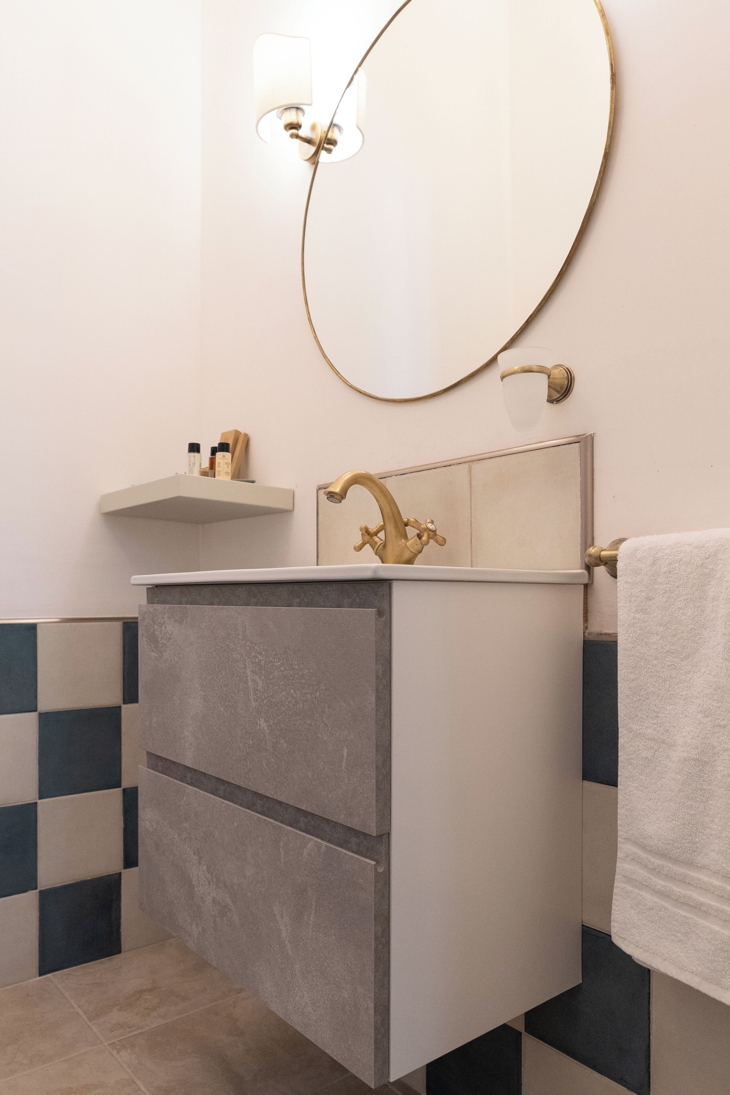 A bathroom with a white sink, gold faucet, and a round mirror.
