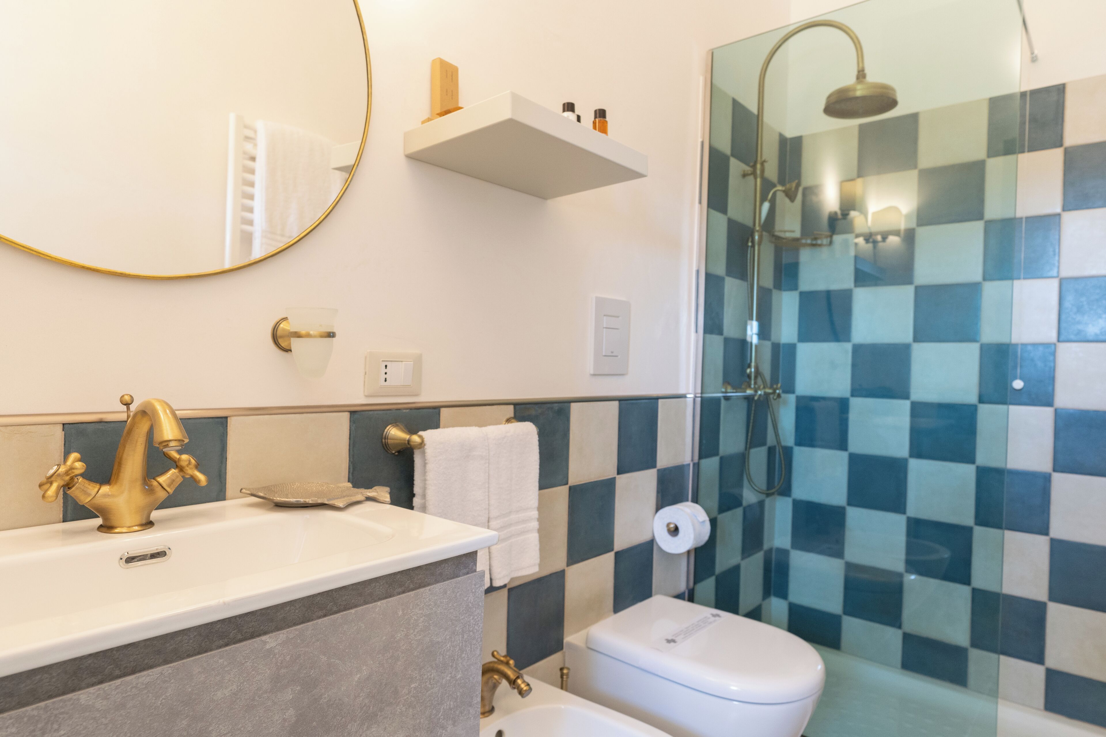 A bathroom with a white sink, gold faucet, and a shower with a glass door.