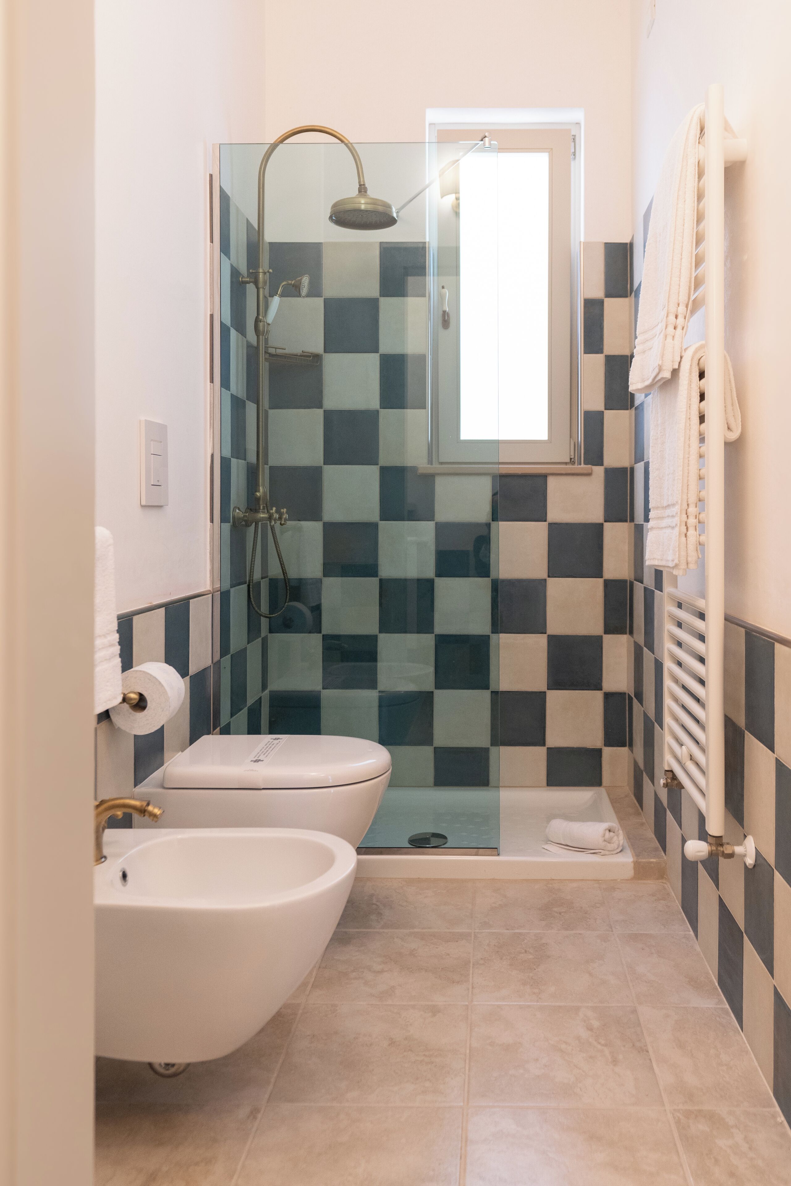 A bathroom with a glass-enclosed shower, a bidet, a toilet, and a towel rack.