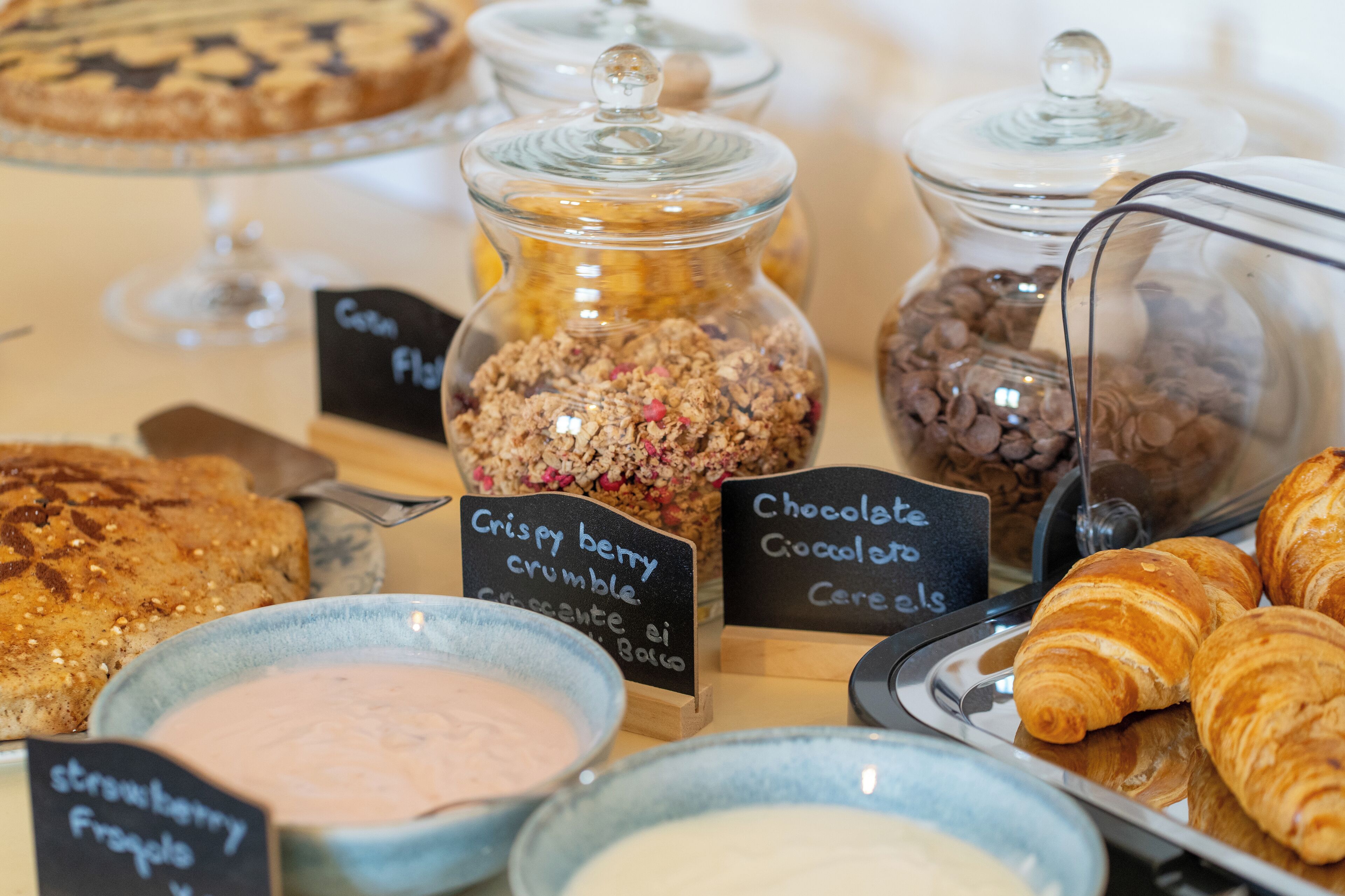 A variety of baked goods and desserts, including a cake, croissants, and jars of cereal and granola.