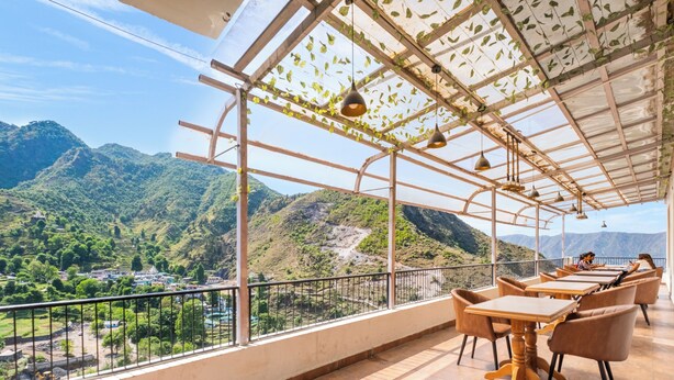 A terrace with tables and chairs, a view of mountains, and a pergola with hanging plants.