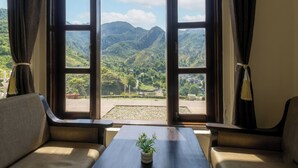 A room with a view of mountains through open doors, a small table with a plant, and two chairs.