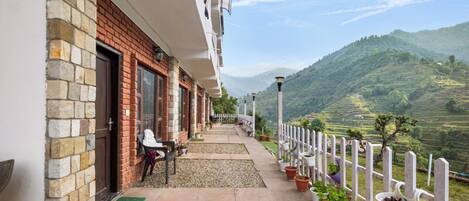 A building with a brick facade, a balcony with potted plants, and a view of green hills.