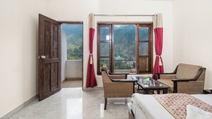 A hotel room with a bed, two chairs, a table, and a balcony with a mountain view.