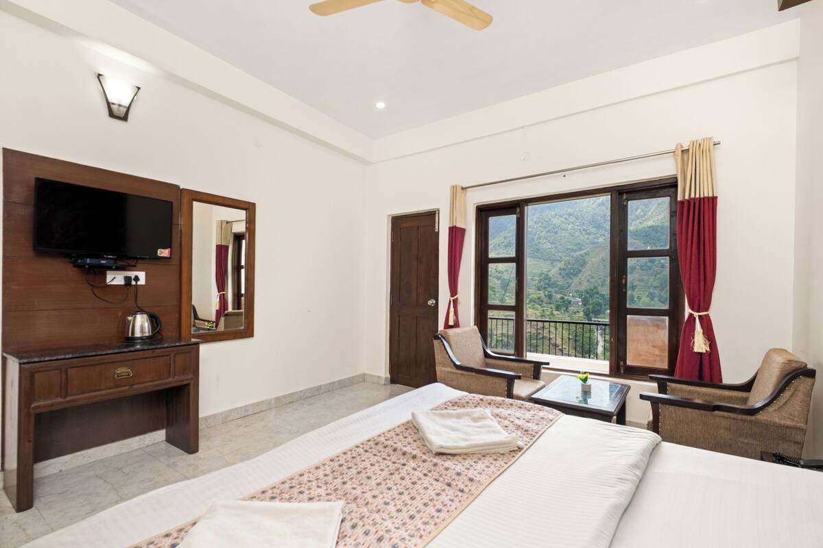 A hotel room with a bed, a TV, a desk, a chair, and a window with a view.