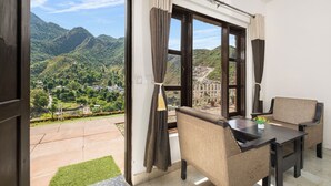 A room with a view of green hills, a table, two chairs, and a window with curtains.