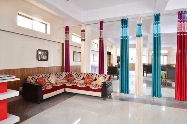 A hotel lobby with a check-in counter, a sofa with patterned cushions, and curtains in various colors. - Hotel Mount Pleasant (Pauri)
