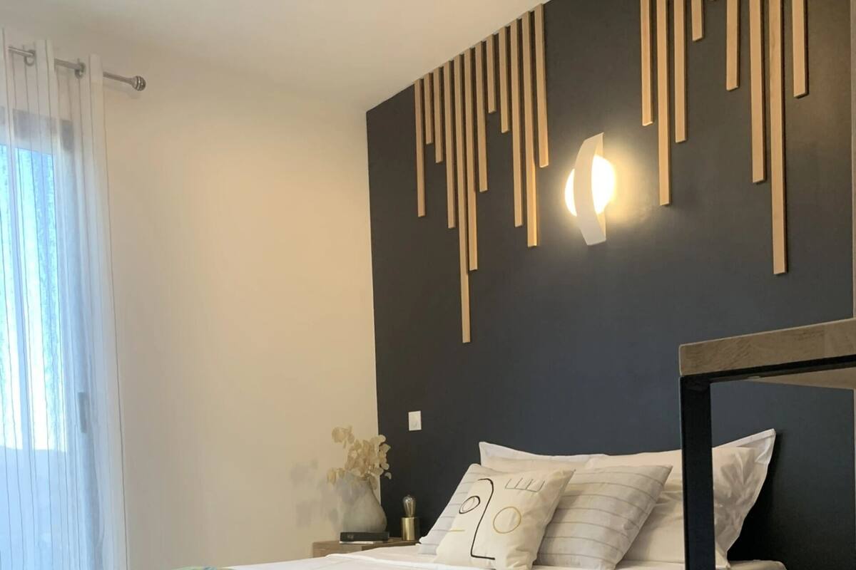 A modern bedroom with a bed, bedside table, and a wall-mounted light fixture.
