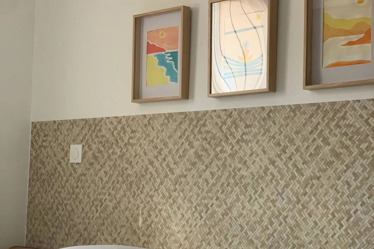 A hotel room with a bed, two pillows, and three framed artworks on the wall.