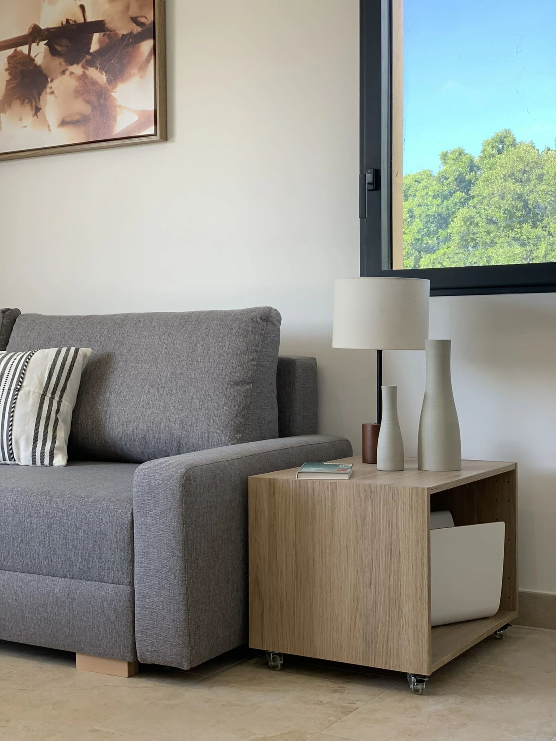 Un soggiorno moderno con un divano grigio, un tavolino con una lampada e un quadro appeso al muro.