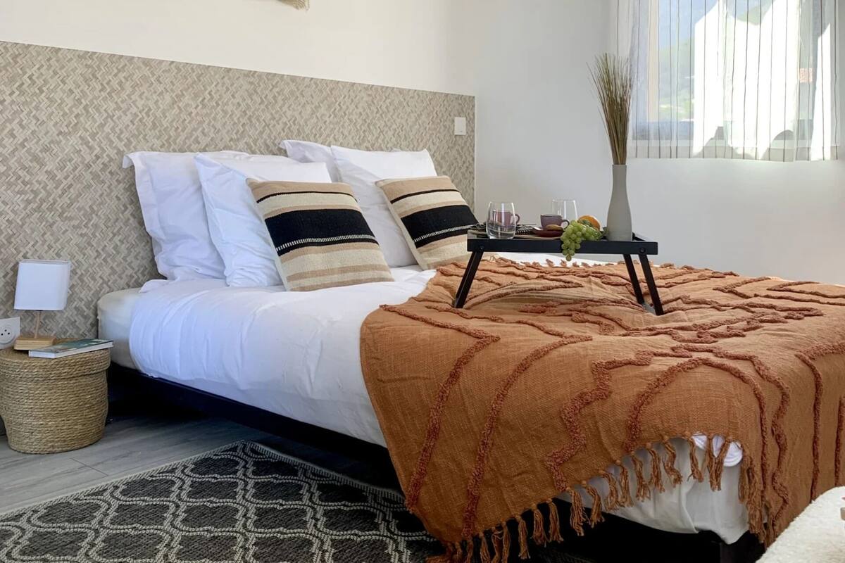 A neatly arranged bedroom with a bed, bedside table, lamp, and a window with curtains.