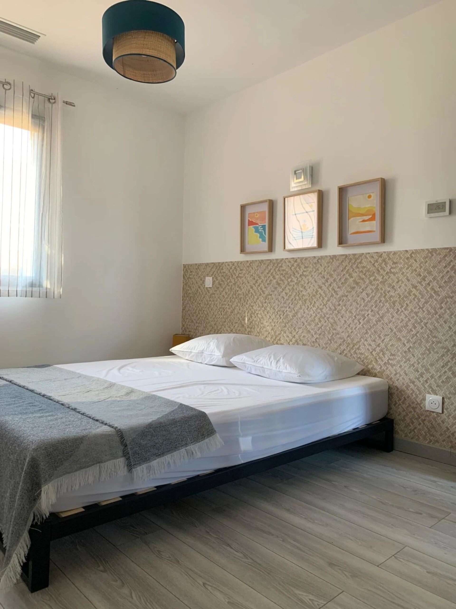 A neatly made bed with white linens and pillows, a patterned wall, and a ceiling light fixture.
