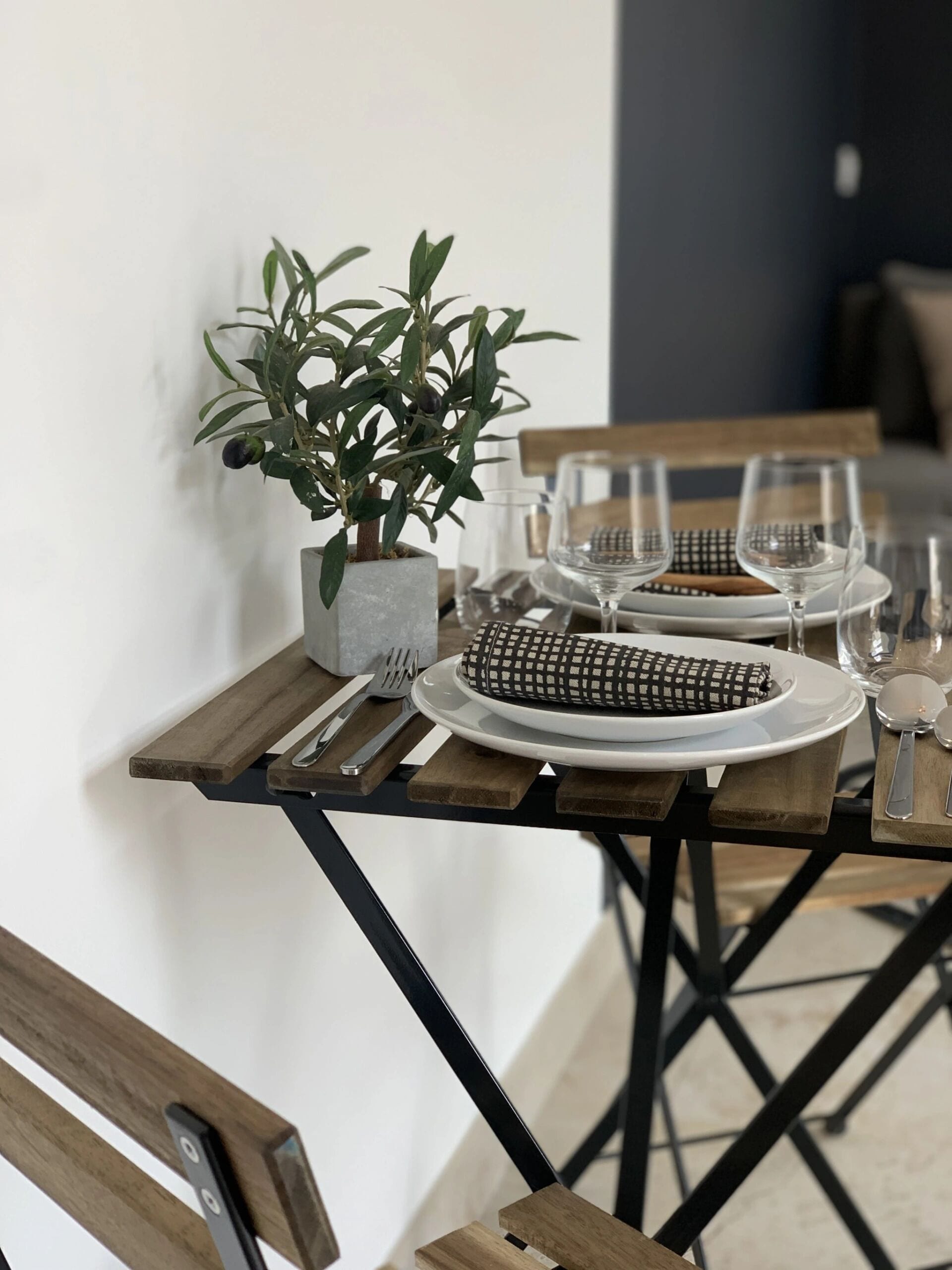 A dining table set with plates, cutlery, and glasses, accompanied by a potted plant.