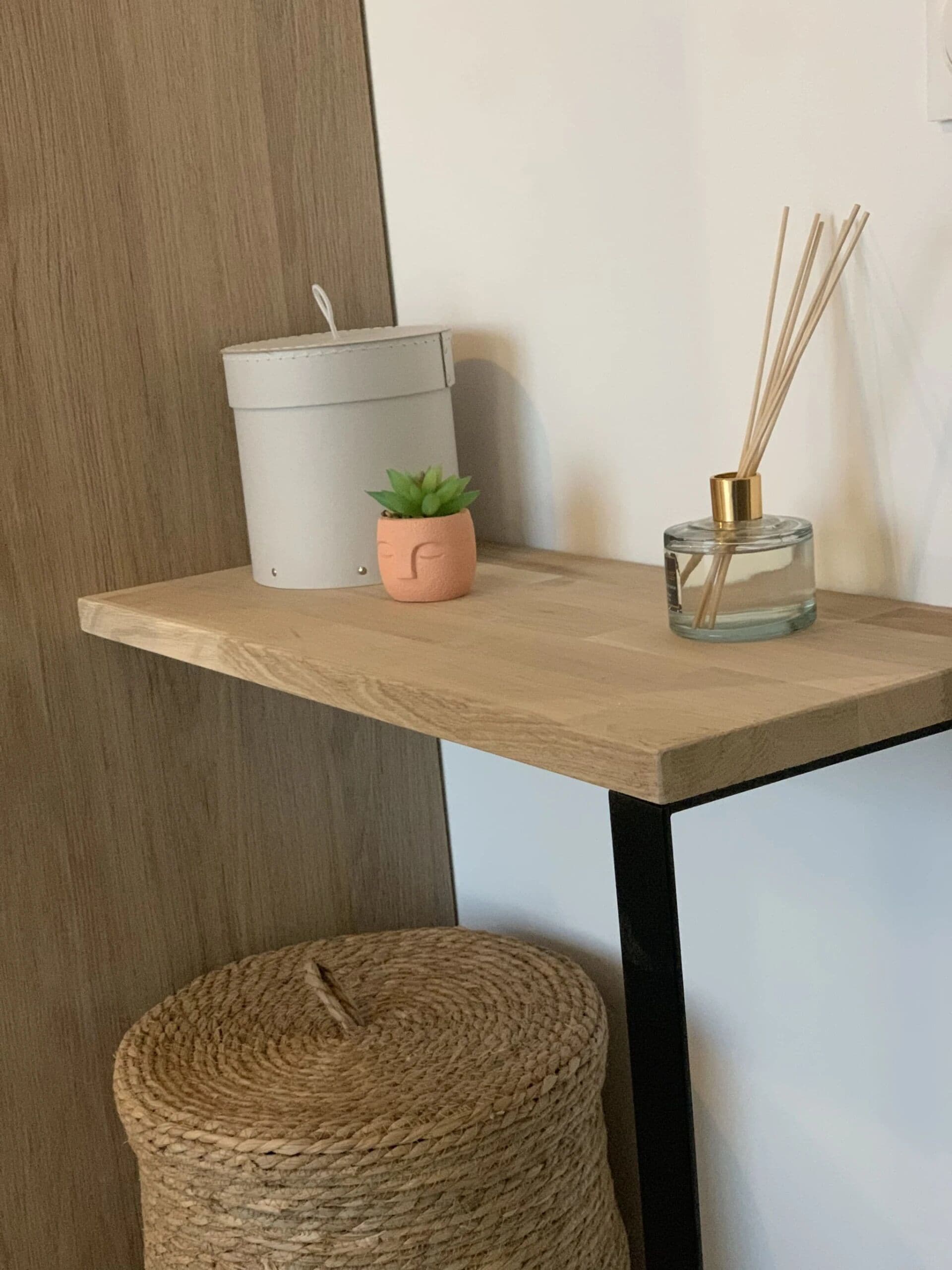 A wooden table with a grey bucket, a small potted plant, and a reed diffuser.