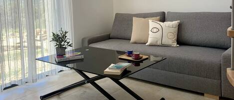 Una sala de estar moderna con un sofá gris, una mesa de centro de vidrio y una planta en maceta.